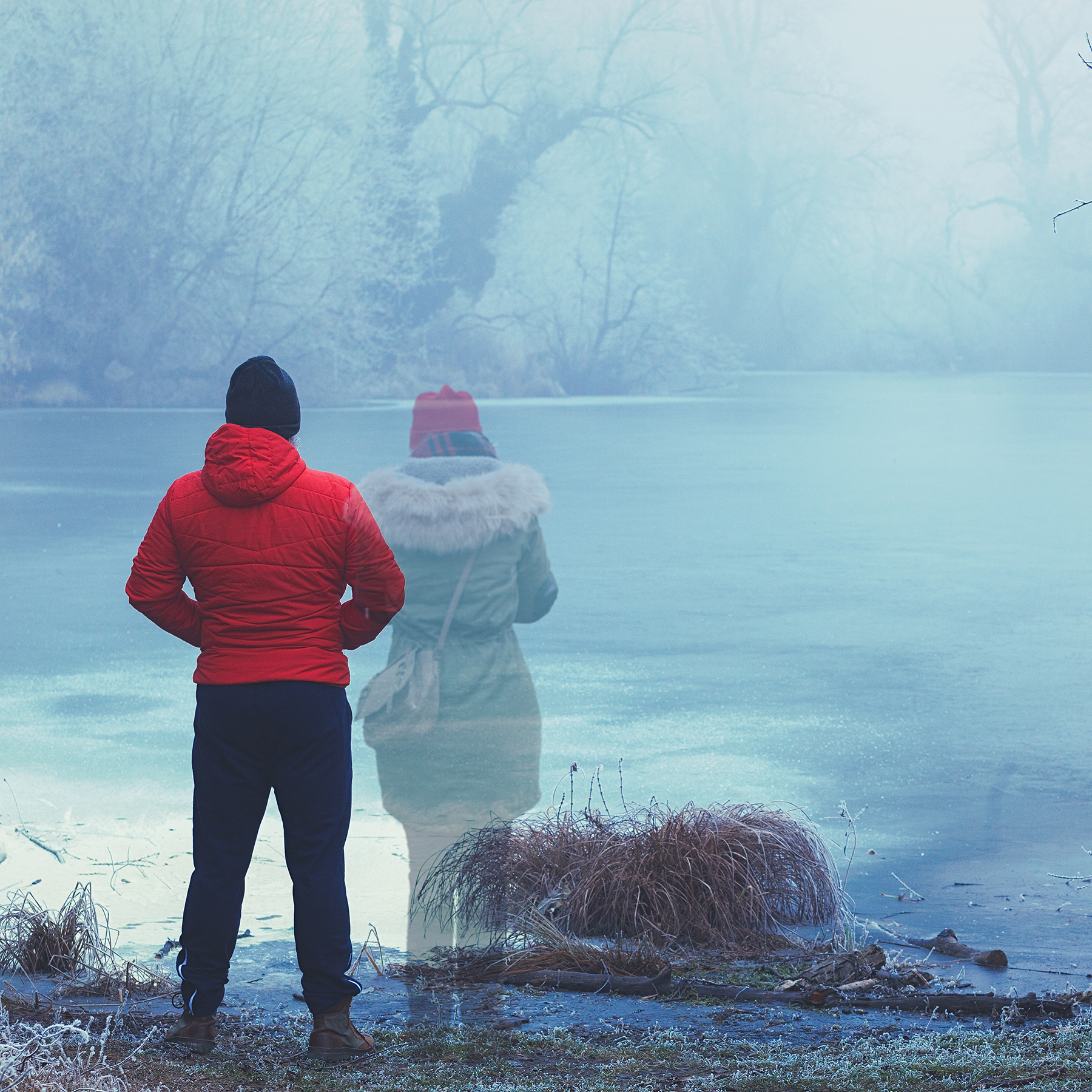 man and woman standing near foggy lake
